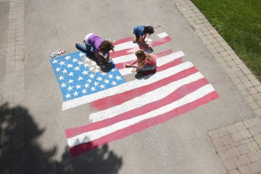 Girls with chalk coloring American flag on sidewalk