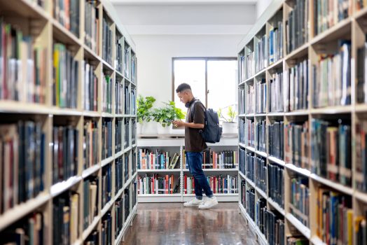 College student walking around the aisles of a library Latin American college student walking around the aisles of a library - education concepts