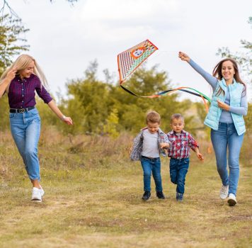 Happy non traditional family of two young mother and their kids launch a kite on nature at sunset.