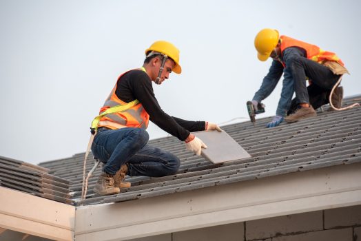 Construction worker wearing safety belt while working on the roof structure of the building on the construction site, Roofer uses a drill and installs concrete roof tiles on the roof.