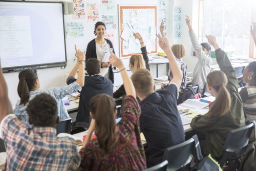 Rear view of teenage students raising hands in classroom Rear view of teenage students raising hands in classroom