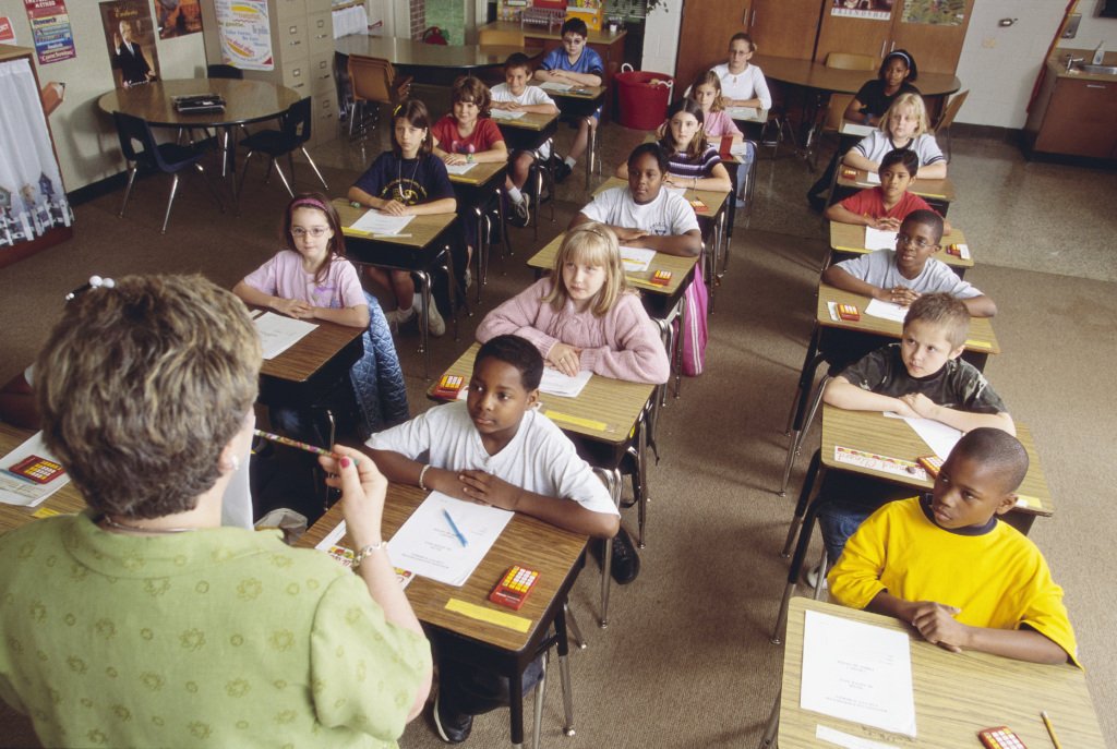 A diverse elementary classroom listens to their teacher during a lesson