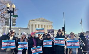 a group of diverse people standing together in front of the U.S. Supreme Court holding rally signs supporting trans rights.