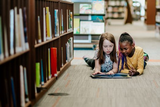Two young girls reading a book on the floor of library Two young girls reading a book on the floor of library